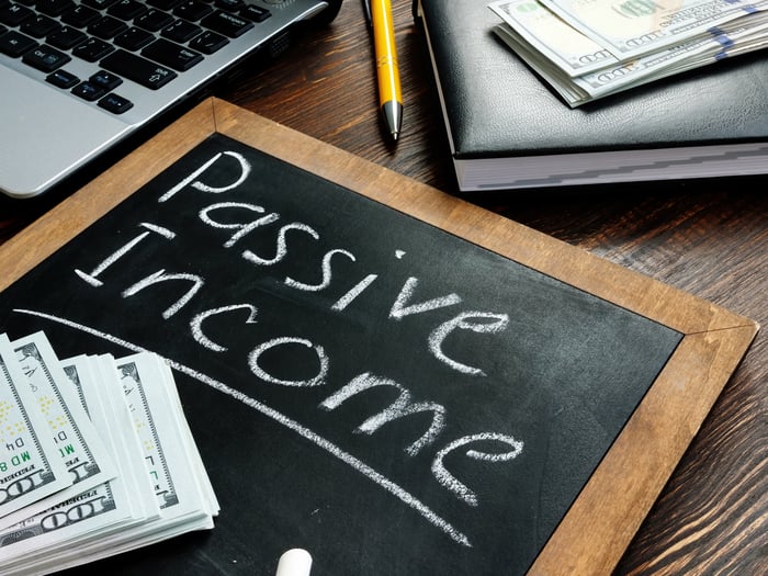 A small chalkboard with passive income written out, near stacks of hundred-dollar bills.