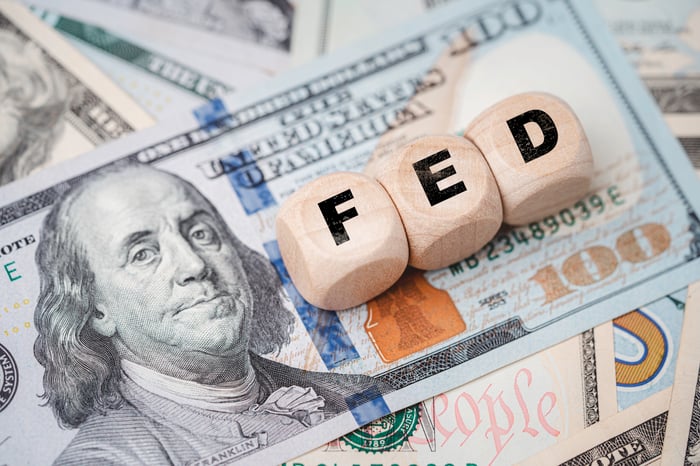 Small wooden blocks labeled "FED" sit on top of a $100 bill.