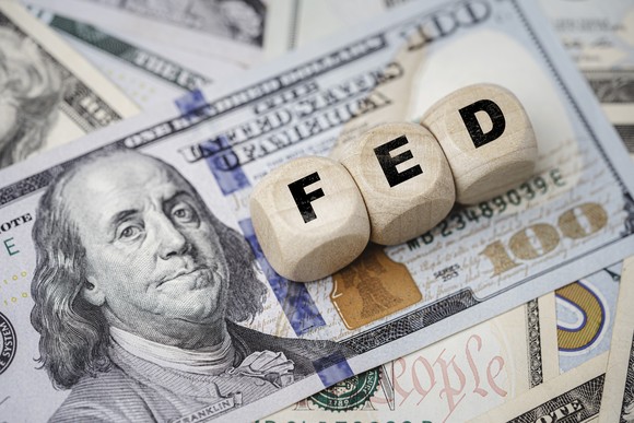 Small wooden blocks labeled "FED" sit on top of a $100 bill.