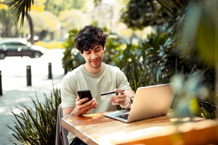A person smiles at their smartphone while holding a credit card in the other hand.