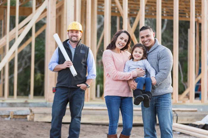 A contractor and a family pose for a group photo on a home construction site.
