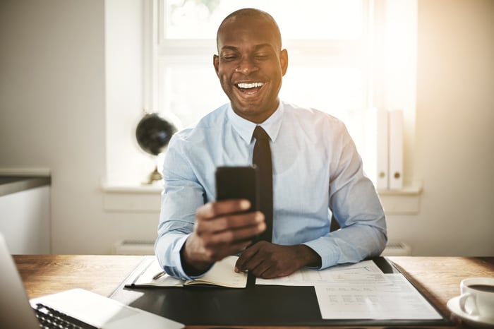 An investor in an office smiles while looking at something on a phone.