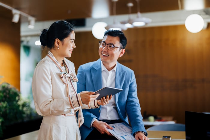 Two investors stand in a lobby while reading from a tablet computer.
