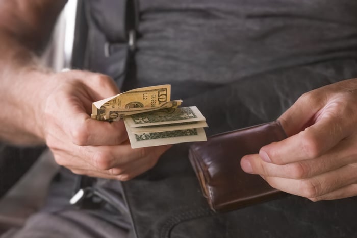 Paper cash bills being pulled out of a wallet.