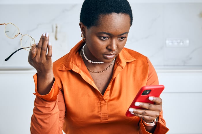 Woman holds glasses in one hand and cellphone in the other.