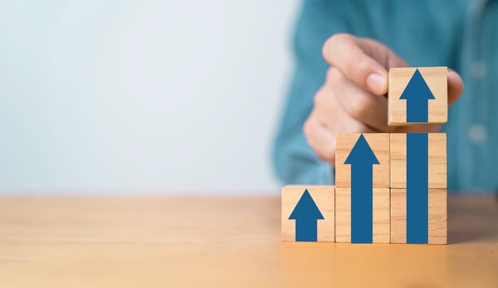 A person stacking blocks that show progressively larger upward-pointing arrows.