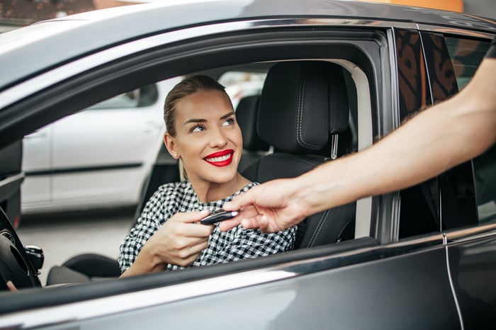 Someone handing keys to person sitting in the driver's seat of a car.