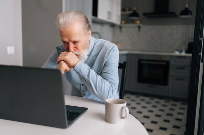 Older person sitting at a kitchen table, looking down at a laptop. 