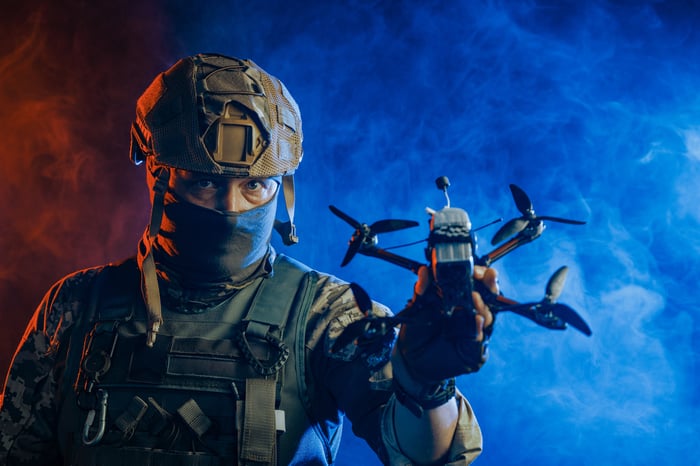 Masked soldier holding quadcopter drone in hand.