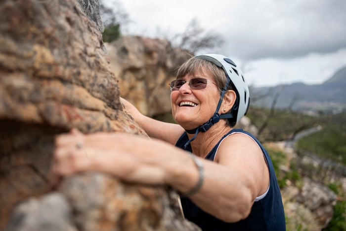 Someone rock climbing while wearing a helmet.
