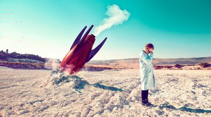 A person in a lab coat is crying next to a crashed rocket.