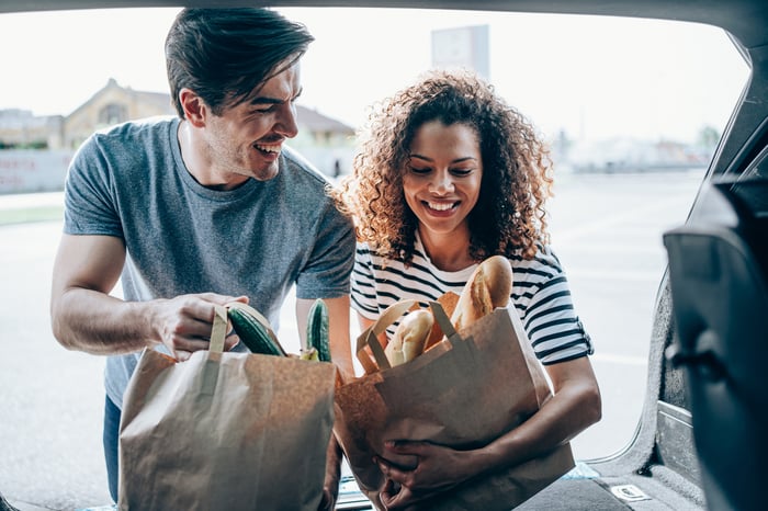 Two people load a car with groceries.
