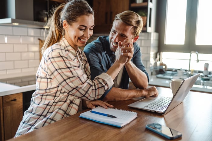 Two people smiling while clasping hands and celebrating financial success at a kitchen table.