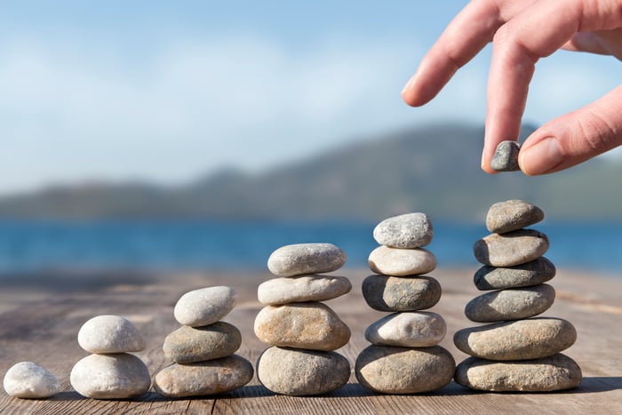 A person stacking stones into increasingly taller towers on a dock by a body of water, illustrating the concept of building passive income.