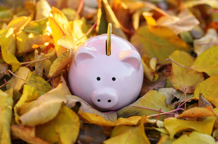 A piggy bank with a coin surrounded by autumn leaves.