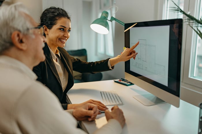 A person in a business suit points to a computer monitor.