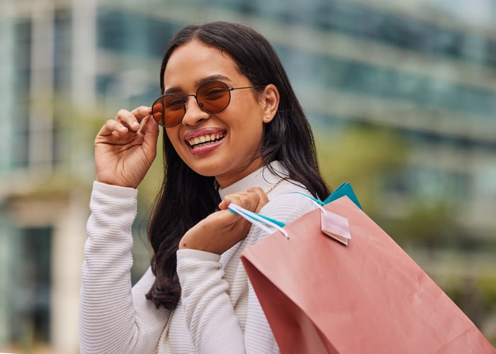 A woman smiling with a shopping bag on her shoulder and sunglasses on. 
