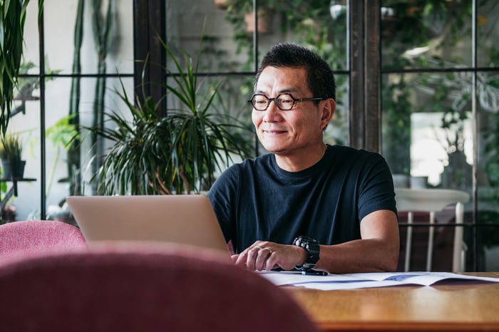 Someone at a table, smiling while using a laptop.