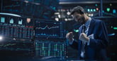 Investor celebrates while standing beside computers showing financial charts.
