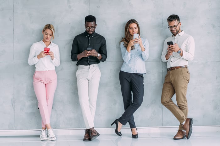 Four young adults on smartphones. 