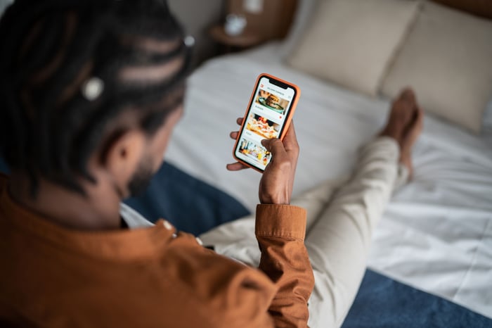 Person installing a mobile app on their smartphone while sitting up on a bed.