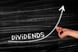 The word dividends on a chalkboard with a person drawing an upward arrow.