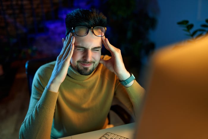 A computer user closing their eyes tightly while rubbing their temples.