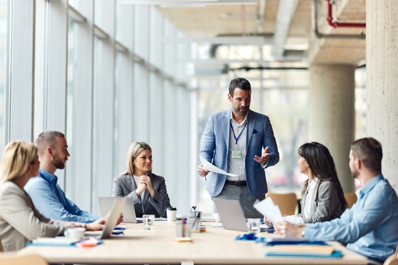 Person presenting to others around an office conference table.