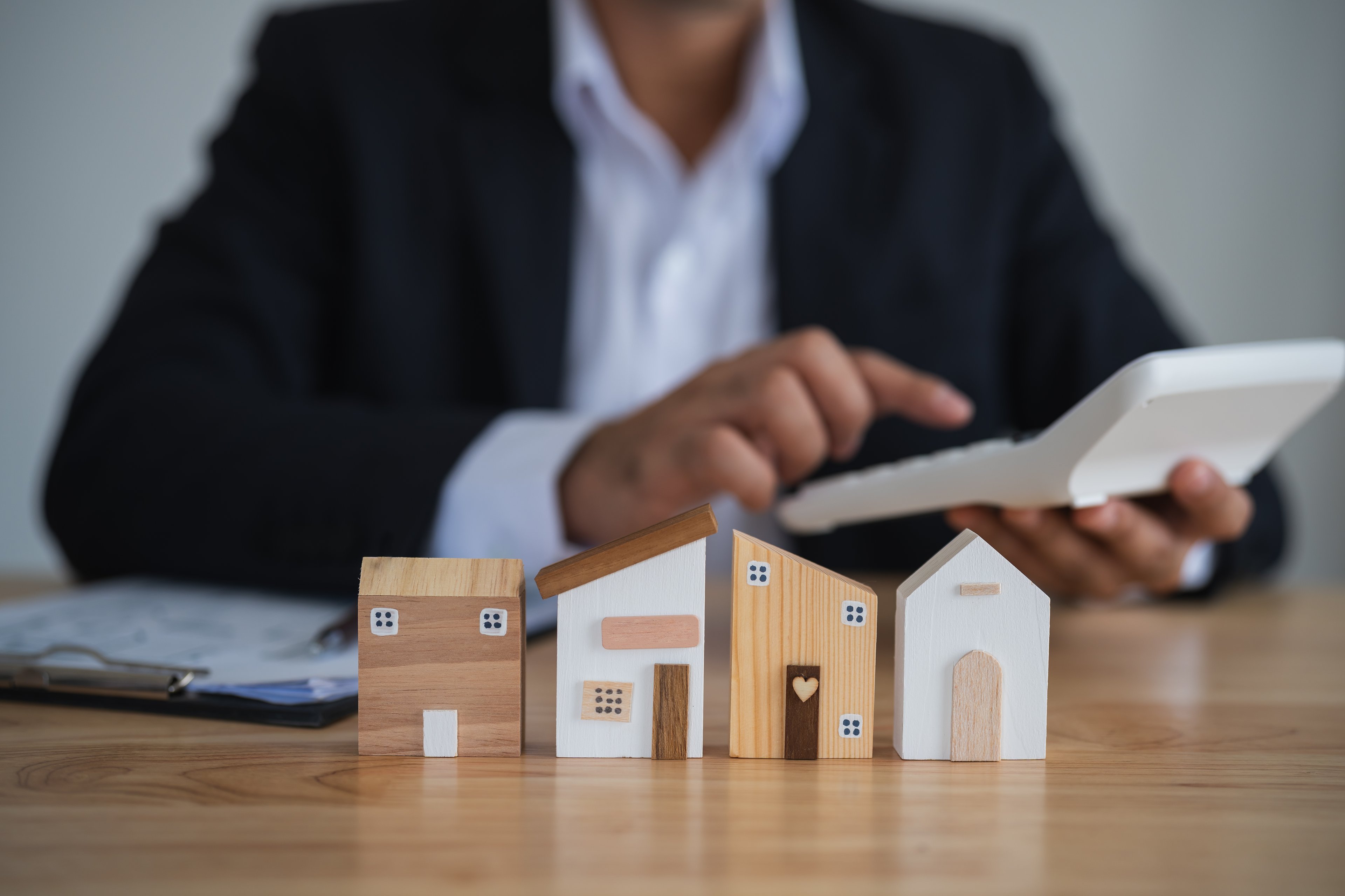 business person at desk uses calculated with miniature houses in front getty