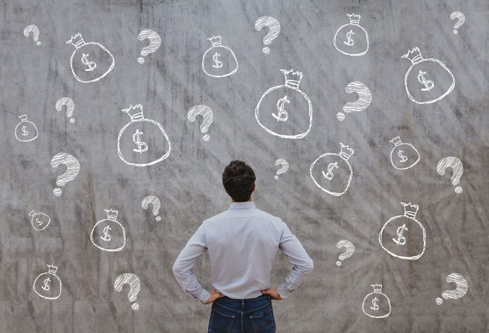 A person looking at chalk drawings of question marks and money bags.