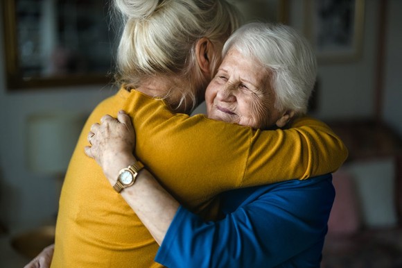 A woman smiles as she receives a hug.