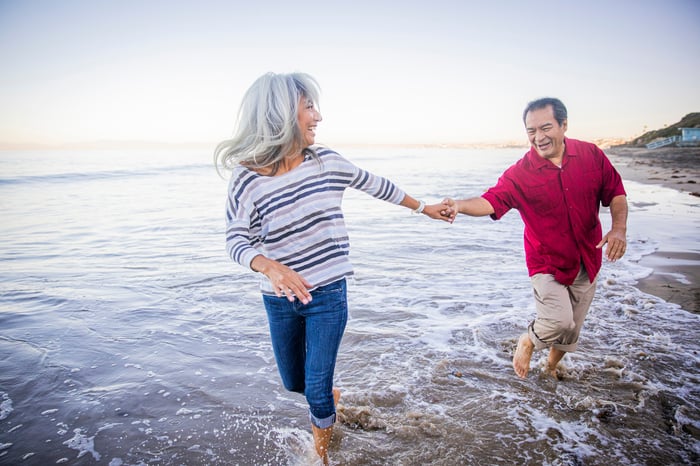 An older couple walking on the beach holding hands.