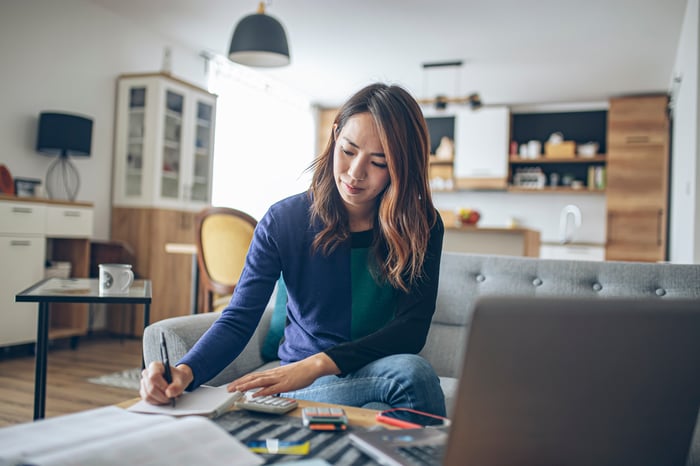 A person with a laptop sitting on a couch and taking notes.