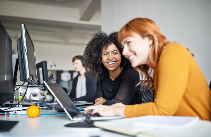 Two cheerful colleagues working together on a laptop in an office.