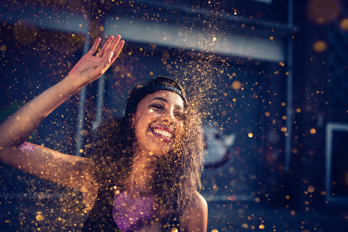 A person smiles while being surrounded by sprinkles of gold dust and flakes.