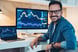 A smiling investor sitting in front of two computer screens, which are displaying stock or cryptocurrency charts
