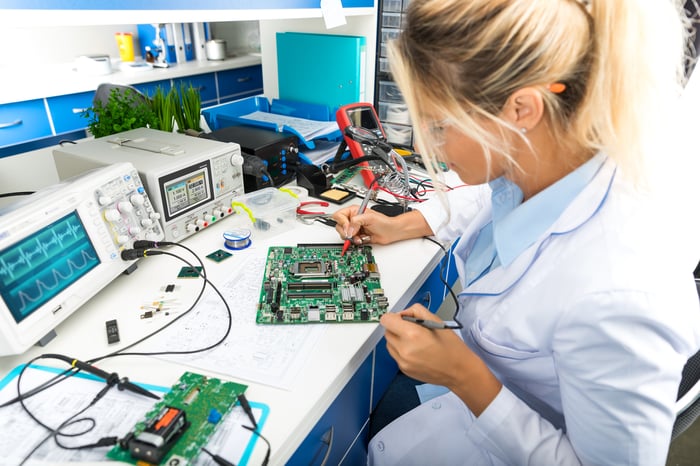 Woman in lab coat tests semiconductor chips on a circuit board.