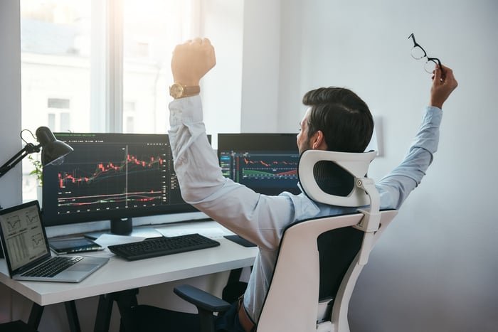 Happy trader looks at financial charts on computers.