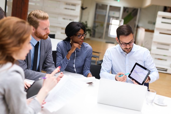 People sitting at a table looking at a chart on tablet.
