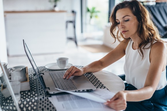 A person looking at papers on a desk and using a laptop.