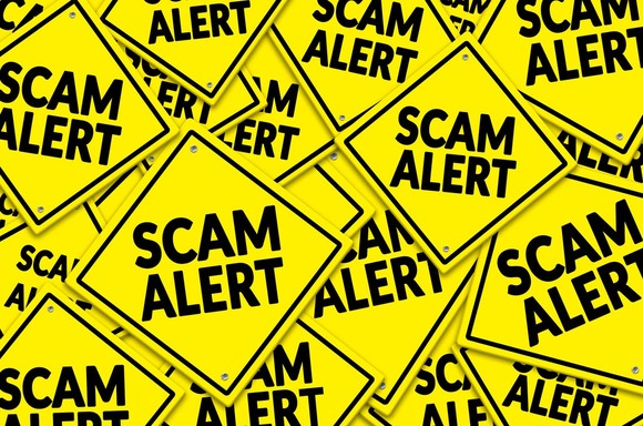 Dozens of bright yellow "Scam Alert" signs stacked on top of each other.