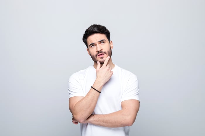 A person stands with their fingers on their chin.