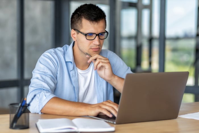 A person deep in thought looking at a laptop.
