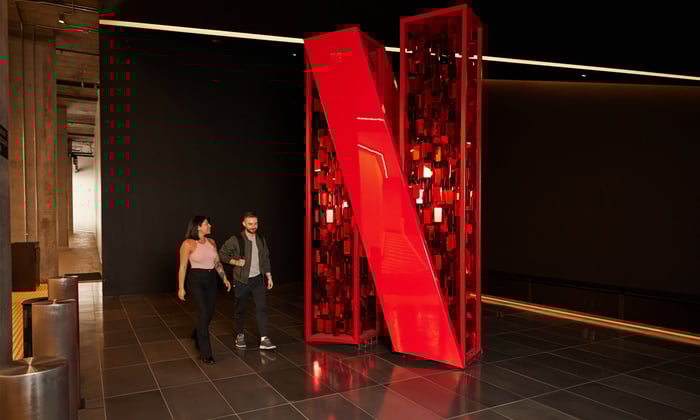 Two people smile while walking by a large Netflix logo in a lobby.