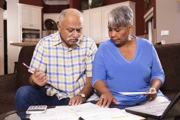 Two people seated on a couch who are examining bills and financial statements placed on a table in front of them.