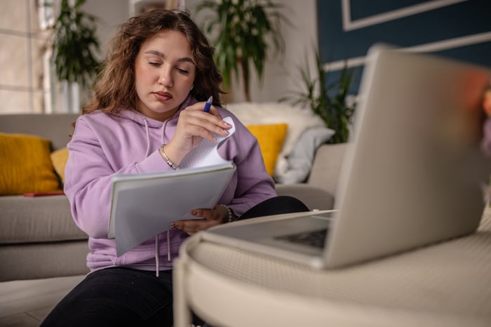 Person looking through notebook in front of laptop.