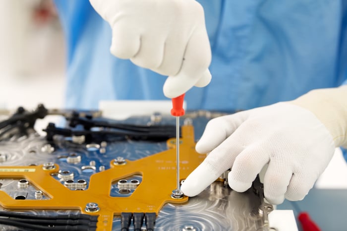 Person wearing gloves working on a circuit board.