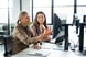 Two_professionals_smiling_while_discussing_something_on_a_desktop_monitor