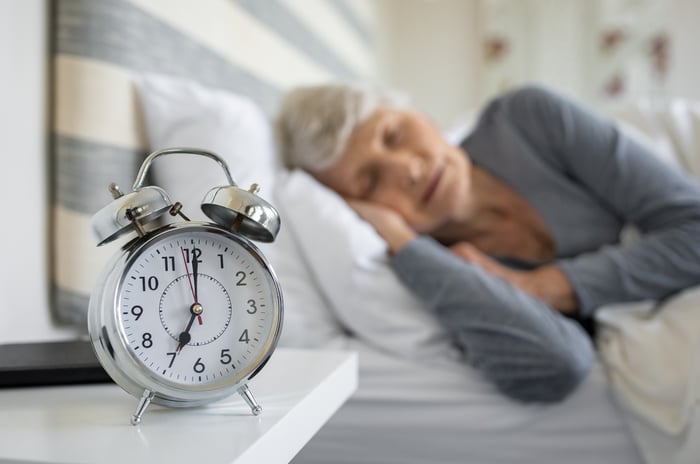 A person in bed sleeping with a clock in the foreground.