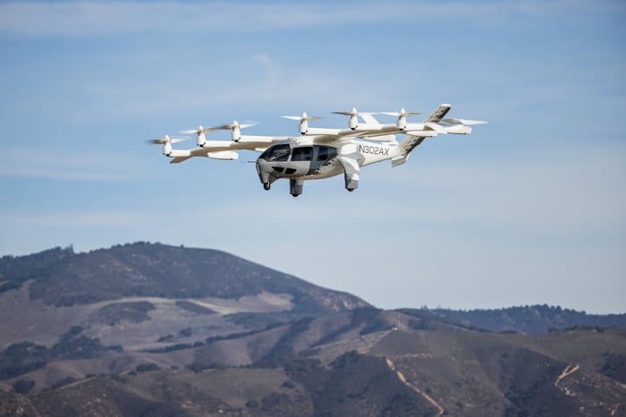 A white Archer Aviation electric vertical takeoff and landing (eVTOL) in flight under a clear blue sky. 